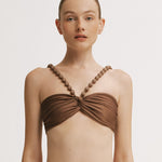 Woman wearing a brown bikini top with beaded straps on a white background.