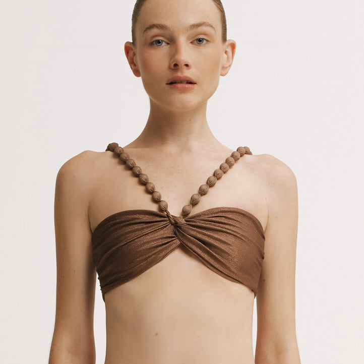 Woman wearing a brown bikini top with beaded straps on a white background.