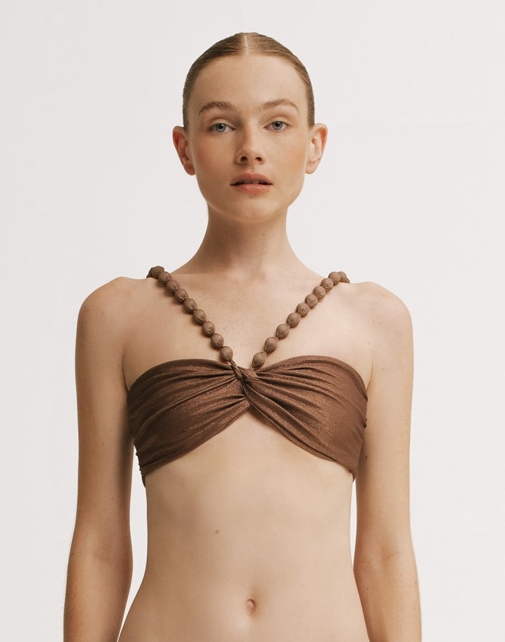 Woman wearing a brown bikini top with beaded straps on a white background.