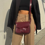 Person wearing a maroon leather bag over one shoulder against a beige wall.