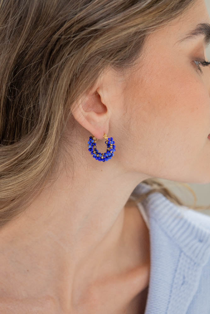 A close-up of a woman's ear wearing a small gold hoop earring adorned with blue beads.