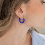A close-up of a woman's ear wearing a small gold hoop earring adorned with blue beads.