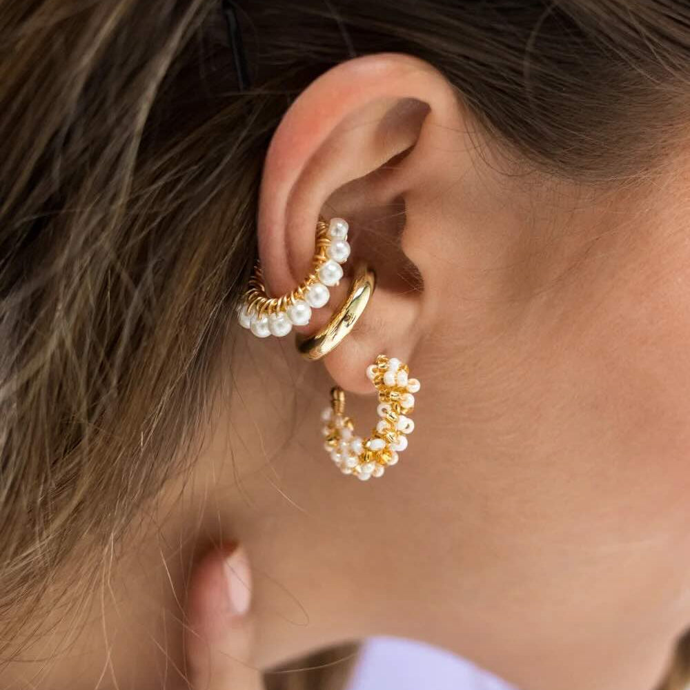 Close-up of a person wearing gold hoop earrings with pearl accents.
