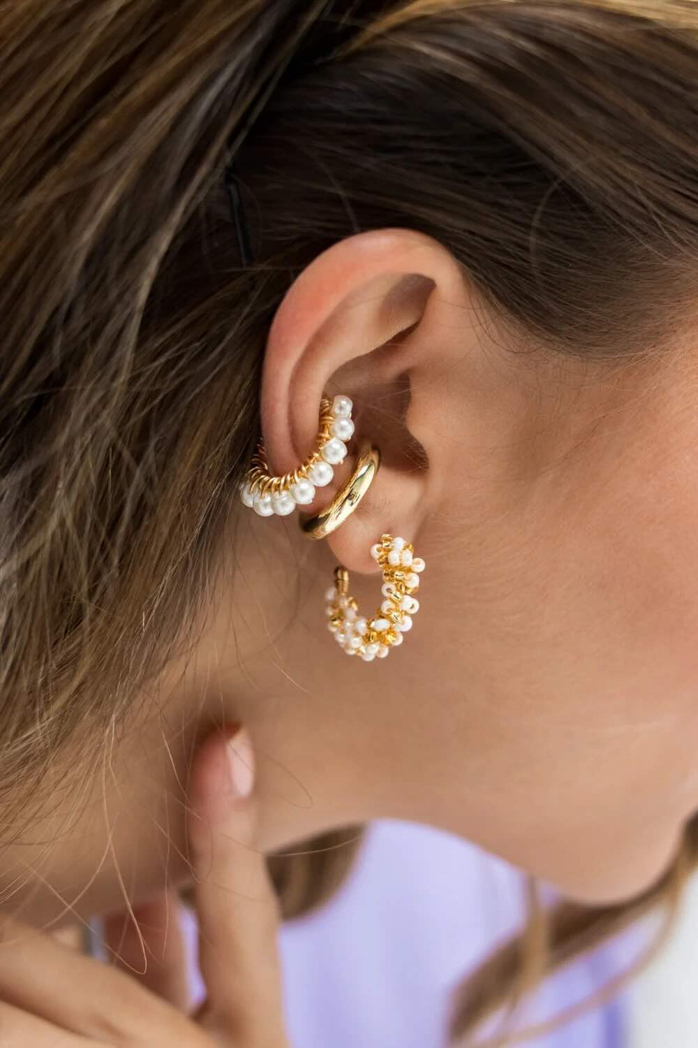 Close-up of a person wearing gold hoop earrings with pearl accents.