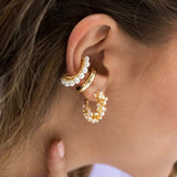 Close-up of a person wearing gold hoop earrings with pearl accents.