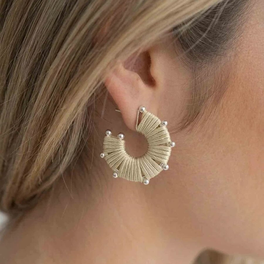 A close-up side profile of a woman wearing a textured, crescent-shaped hoop earring in a light beige or cream tone with small pearl-like beads at the tips.
