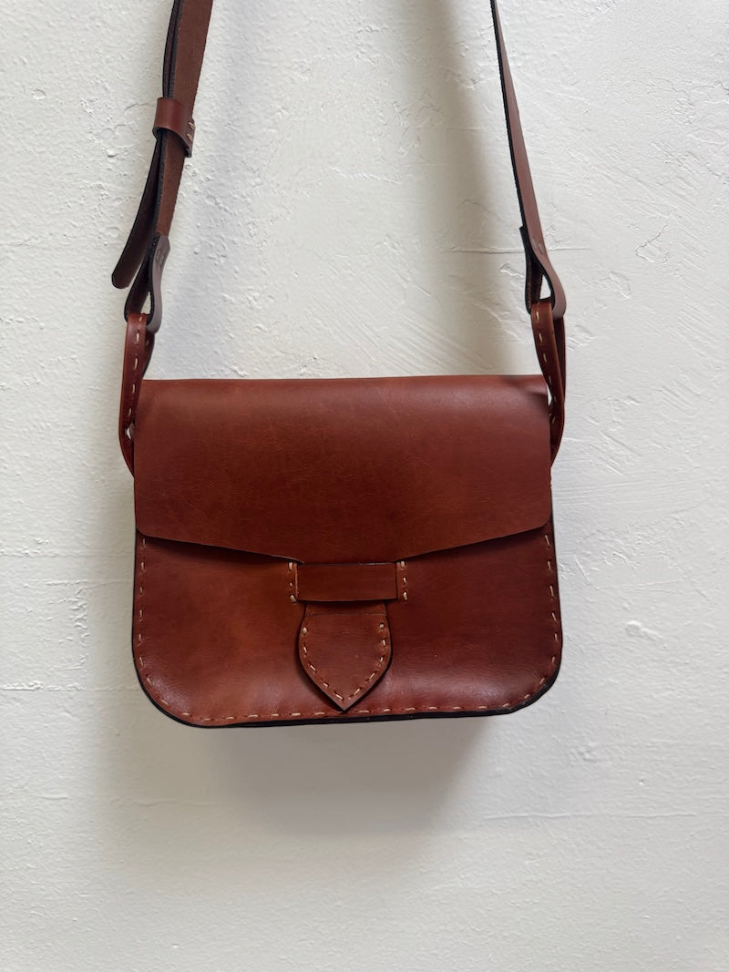 Cognac brown leather crossbody bag on a white textured background