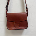 Cognac brown leather crossbody bag on a white textured background