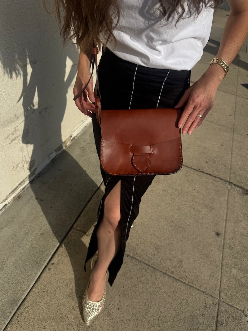 Person holding a brown leather bag on a sidewalk