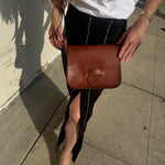 Person holding a brown leather bag on a sidewalk