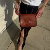 Person holding a brown leather bag on a sidewalk