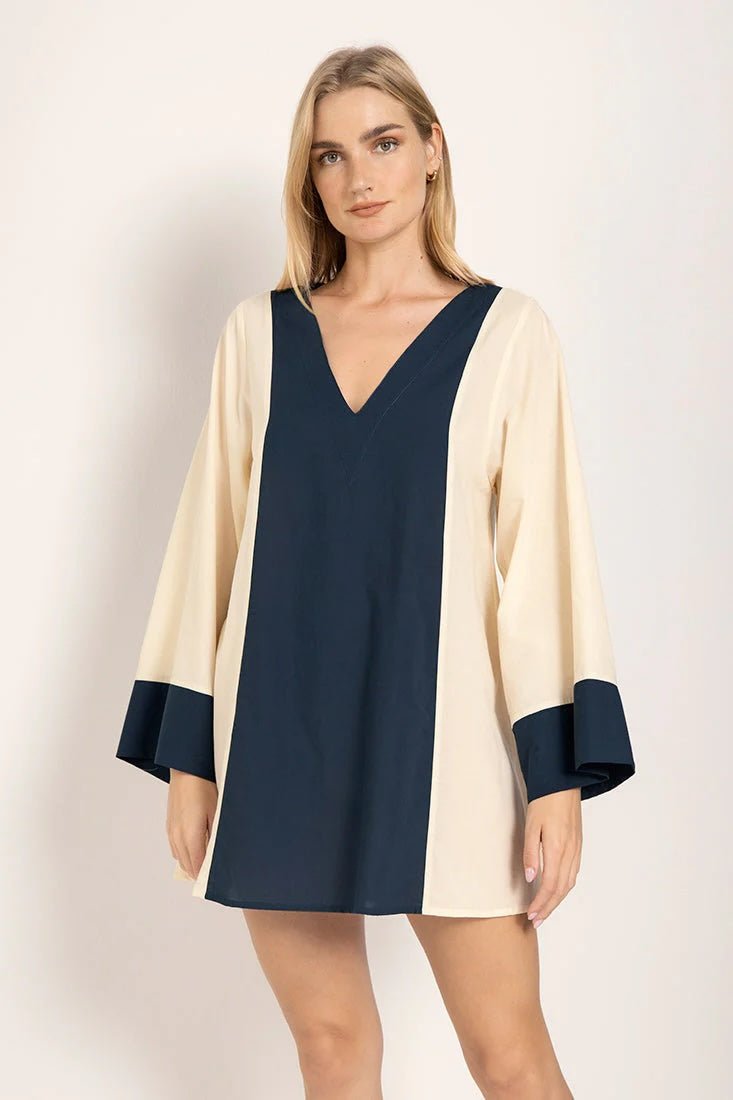 Image of a model wearing a long sleeve color-block dress with white and navy tones. She's looking at the camera and standing against a white background. The purpose of this image is to highlight the dress.