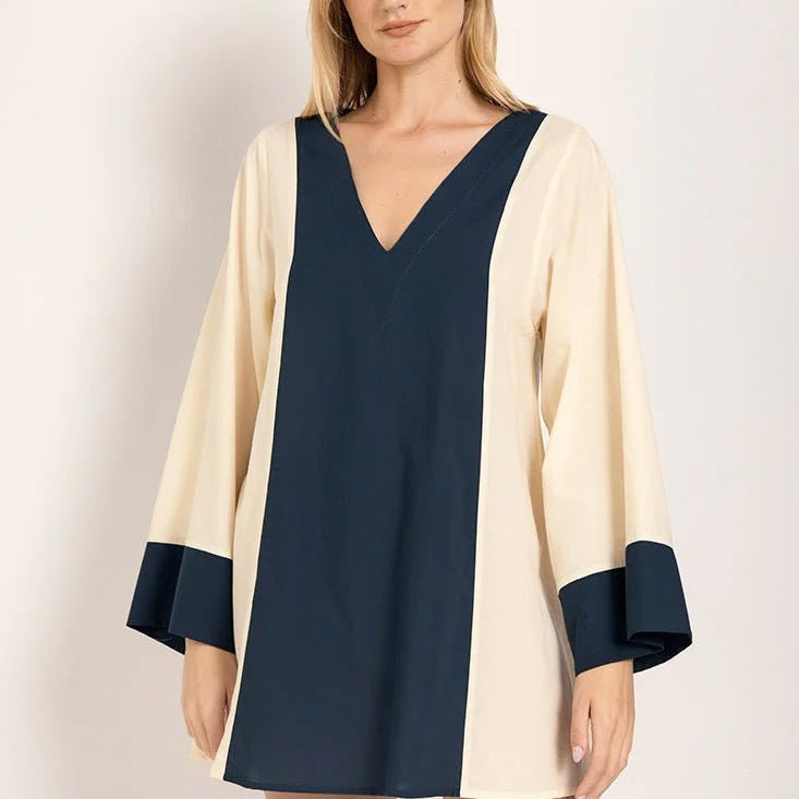 Image of a model wearing a long sleeve color-block dress with white and navy tones. She's looking at the camera and standing against a white background. The purpose of this image is to highlight the dress.