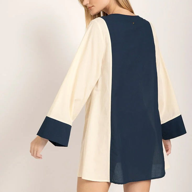 Image of the back of a model wearing a long sleeve color-block dress with white and navy tones. She's looking to the side and standing against a white background. The purpose of this image is to highlight the dress.