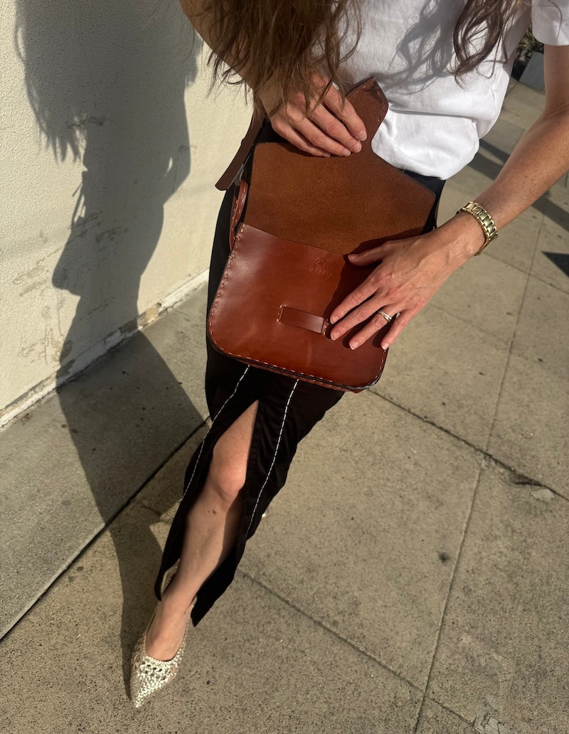 Person holding a brown leather clutch on a sidewalk