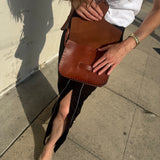 Person holding a brown leather clutch on a sidewalk