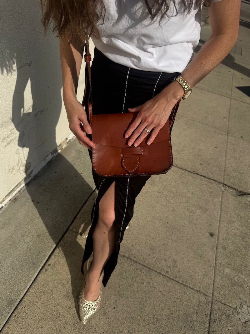 Person holding a brown leather bag on a sidewalk