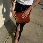 Person holding a brown leather bag on a sidewalk