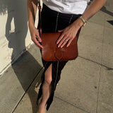 Person holding a brown leather bag on a sidewalk