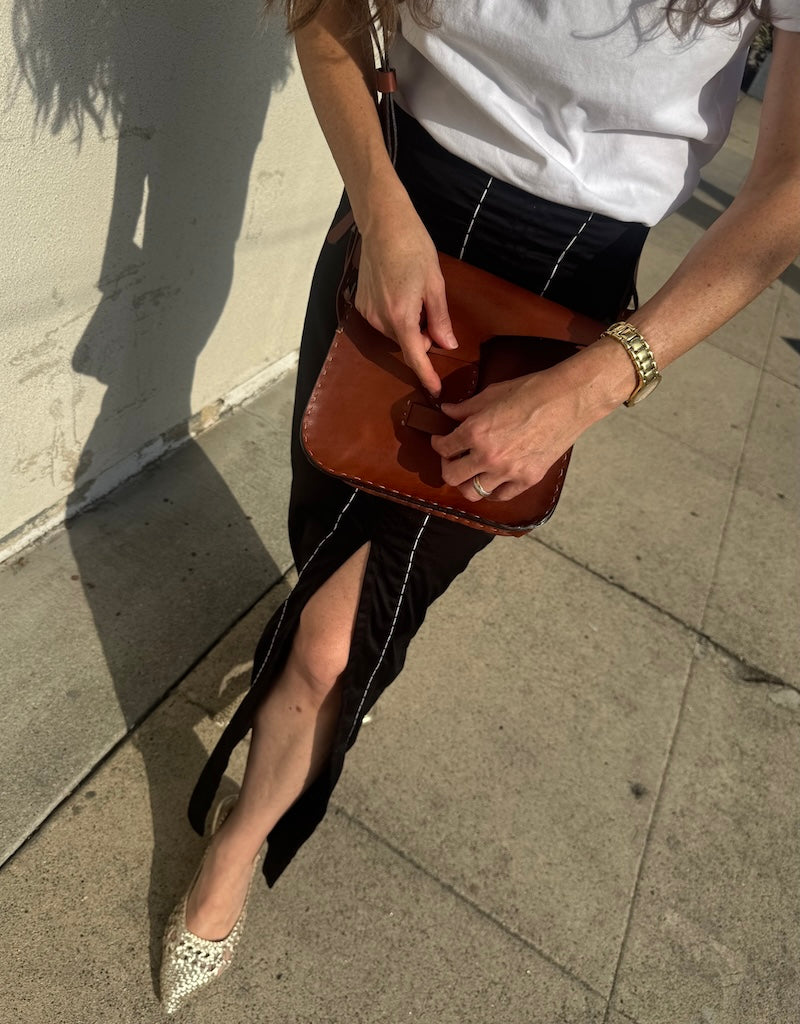 Person holding a brown leather bag on a sidewalk