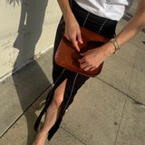 Person holding a brown leather bag on a sidewalk