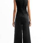 Back of a woman wearing a black jumpsuit with a cutout on the front. She's against a white background. The purpose of this image is to highlight the jumpsuit, which is for sale at EVAMAIA Boutique, in Studio City, CA.