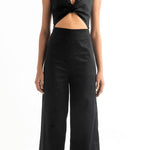 Woman wearing a black jumpsuit with a cutout on the front. She's against a white background. The purpose of this image is to highlight the jumpsuit, which is for sale at EVAMAIA Boutique, in Studio City, CA.