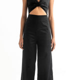 Woman wearing a black jumpsuit with a cutout on the front. She's against a white background. The purpose of this image is to highlight the jumpsuit, which is for sale at EVAMAIA Boutique, in Studio City, CA.