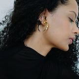 Woman wearing an assortment of gold and silver hoop earrings with a plain background.