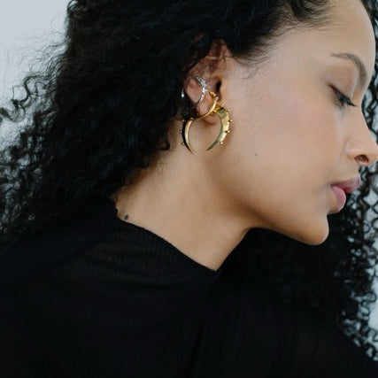 Woman wearing an assortment of gold and silver hoop earrings with a plain background.