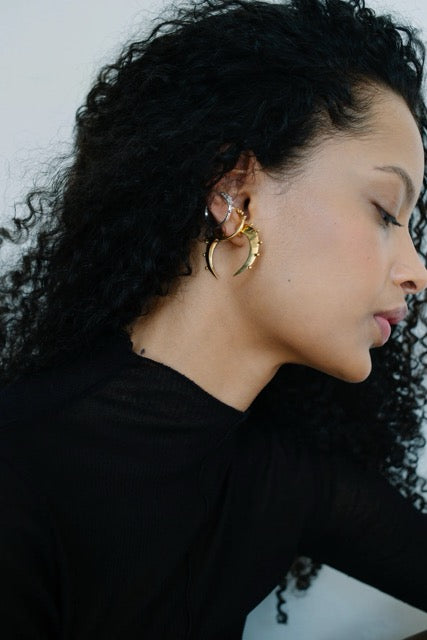 Woman wearing an assortment of gold and silver hoop earrings with a plain background.