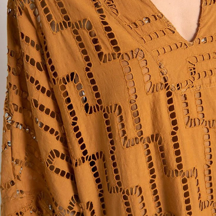 Close up image of a woman wearing a rust-colored dress. The purpose of this image is to show the embroidery details of the tunic dress.