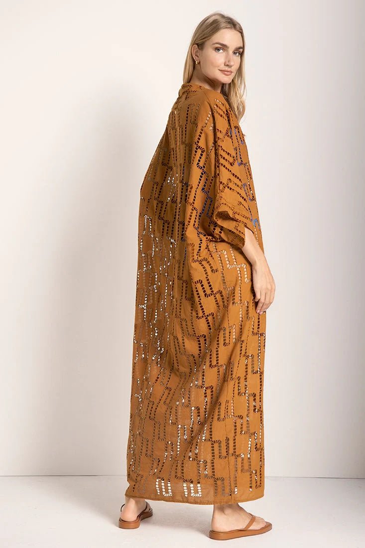 Woman wearing a rust-colored dress. She's standing against a white wall and looking at the photographer. The purpose of this image is to highlight the tunic dress.