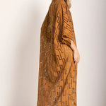 Woman wearing a rust-colored dress. She's standing against a white wall and looking at the photographer. The purpose of this image is to highlight the tunic dress.