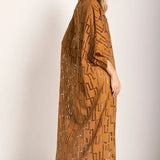 Woman wearing a rust-colored dress. She's standing against a white wall and looking at the photographer. The purpose of this image is to highlight the tunic dress.