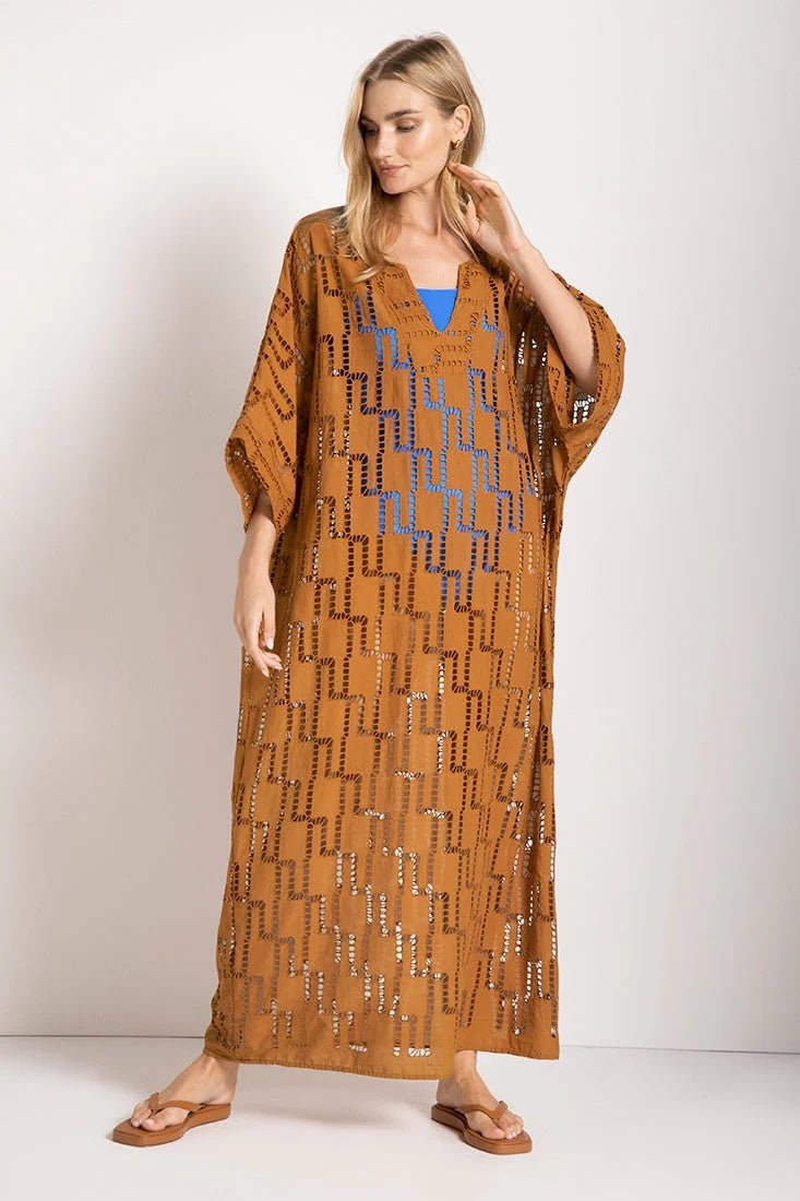 Woman wearing a rust-colored dress. She's standing against a white wall and looking at the photographer. The purpose of this image is to highlight the tunic dress.