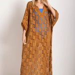 Woman wearing a rust-colored dress. She's standing against a white wall and looking at the photographer. The purpose of this image is to highlight the tunic dress.