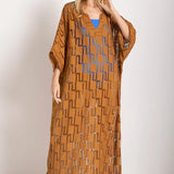Woman wearing a rust-colored dress. She's standing against a white wall and looking at the photographer. The purpose of this image is to highlight the tunic dress.