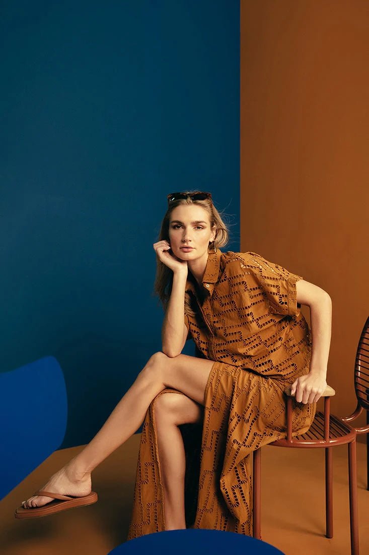 Image of a woman wearing sunglasses on top of her head and an embroidered set. She is sitting against a brown and blue background. She's looking at the camera. The purpose of this image is to highlight the skirt and shirt.