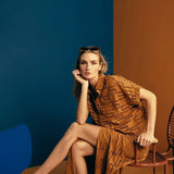 Image of a woman wearing sunglasses on top of her head and an embroidered set. She is sitting against a brown and blue background. She's looking at the camera. The purpose of this image is to highlight the skirt and shirt.