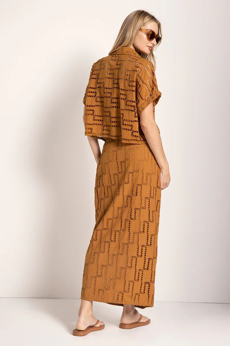 Image of a woman wearing an embroidered set. She is looking to the side and giving her back to the camera. The purpose of this image is to highlight the skirt and shirt.