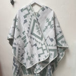 Gray, green and white geometric patterned poncho draped over a hanger against a white wall.
