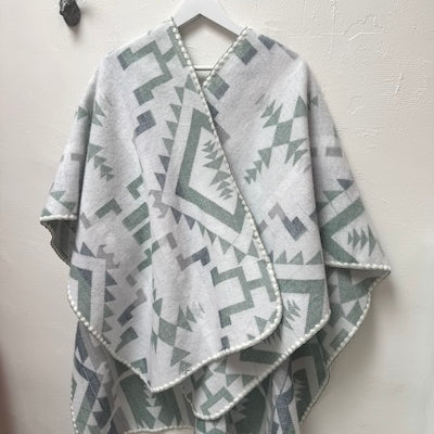 Gray, green and white geometric patterned poncho draped over a hanger against a white wall.