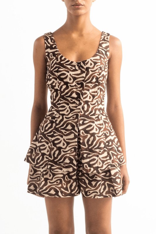 Woman wearing a brown vest with matching shorts. Her face is cutoff and the background is white. This image helps us notice the fit of the clothing described.