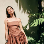 Image of a model wearing a brown dress with Spaghettin straps. She's standing against a wall and seems tired.