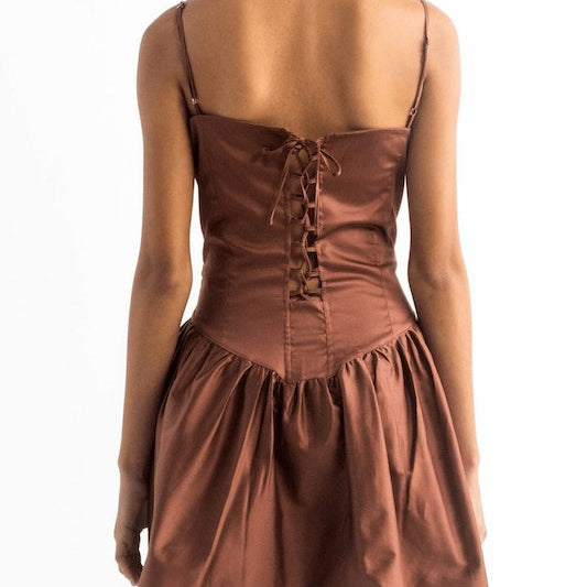 Image of the back of a woman wearing a brown dress with spaghetti straps and a tie closure on the back. She's against a white background and her head is cut out. The purpose of this image is to show the dress.