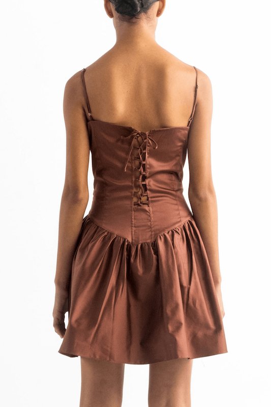 Image of the back of a woman wearing a brown dress with spaghetti straps and a tie closure on the back. She's against a white background and her head is cut out. The purpose of this image is to show the dress.