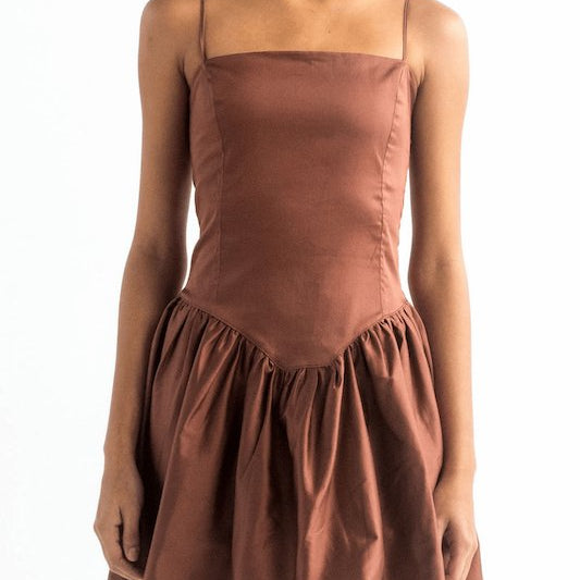 Image of a woman wearing a brown dress with spaghetti straps. She's against a white background and her head is cut out. The purpose of this image is to show the dress. 