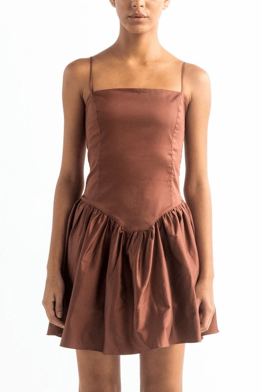 Image of a woman wearing a brown dress with spaghetti straps. She's against a white background and her head is cut out. The purpose of this image is to show the dress. 