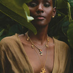 Woman wearing gold necklaces with palm tree pendants in a natural setting